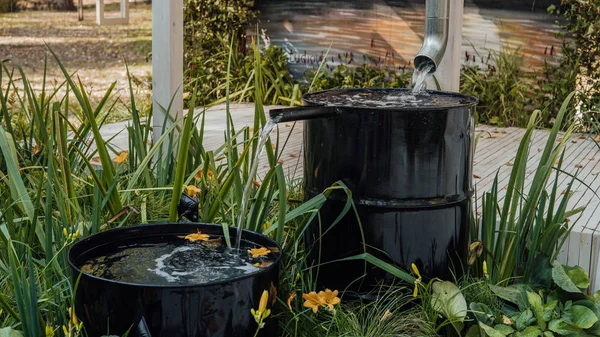 Rainwater flows from a drainage pipe into the metal barrel